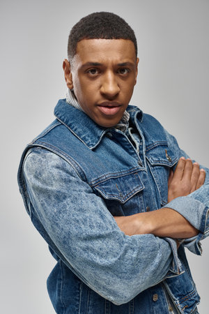 handsome emotional african american man in denim outfit posing on white backdrop, fashion conceptの写真素材
