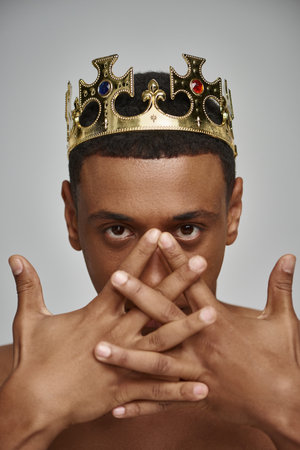 alluring african american man in golden crown posing topless with hands near face, fashion conceptの写真素材