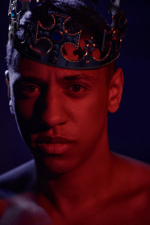 portrait of sexy shirtless african american man in golden crown posing in lights, fashion concept