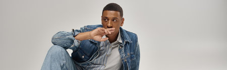 good looking african american man in trendy denim outfit sitting on floor, fashion concept, banner