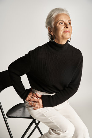portrait of happy middle aged business woman in elegant attire and hoop earrings sitting on chairの写真素材