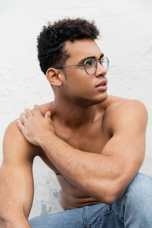 Young and curly cuban man with athletic body wearing jeans and stylish round-shaped eyeglassesの写真素材
