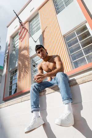 cuban man with muscular body posing in baseball cap and jeans on street in Miami in summer dayの写真素材