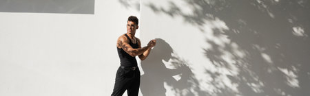 Muscular cuban man in eyeglasses and black outfit looking away while standing near building, banner