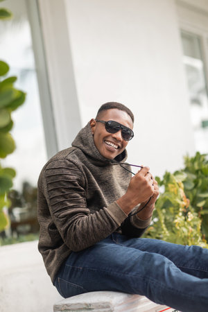 happy african american man in hoodie and sunglasses sitting on street in Miamiの写真素材