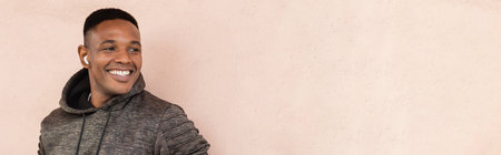 cheerful african american man in wireless earphone standing near wall, bannerの写真素材