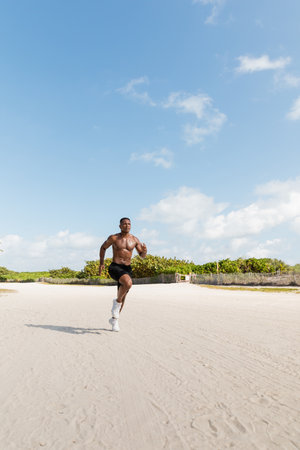 shirtless african american sportsman in shorts running on sand in Miami beachの写真素材
