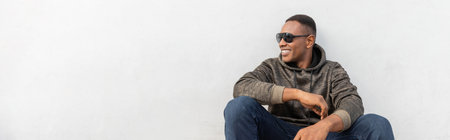 happy african american man in stylish sunglasses sitting near white wall, bannerの写真素材