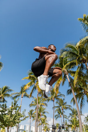 low angle view of shirtless african american sportsman in shorts jumping near palm trees in Miamiの写真素材