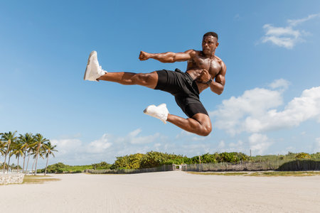 muscular african american man jumping while exercising in Miami beachの写真素材