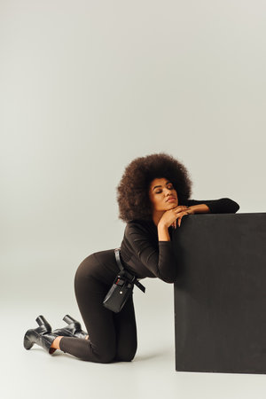 beautiful african american female model in black bodysuit posing next to black cube, fashion conceptの写真素材