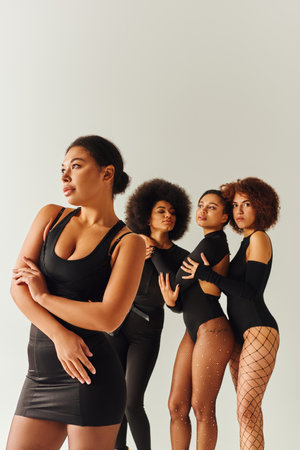 appealing sexy african american women in black stylish bodysuits posing together, fashion conceptの写真素材