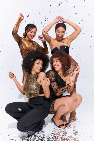 stylish attractive african american women partying under confetti rain sitting on floor, fashionの写真素材