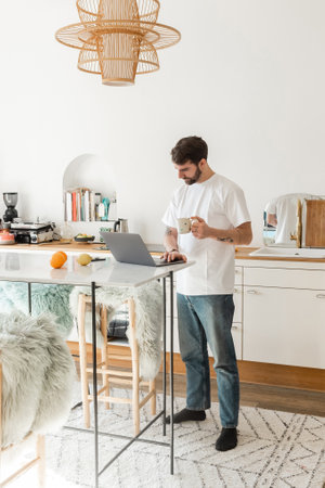 freelancer in white t-shirt and jeans holding cup of coffee and working on laptop at homeの写真素材