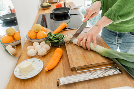 Cropped tattooed man cutting fresh leek near eggs, butter and food on worktop in modern kitchenの写真素材