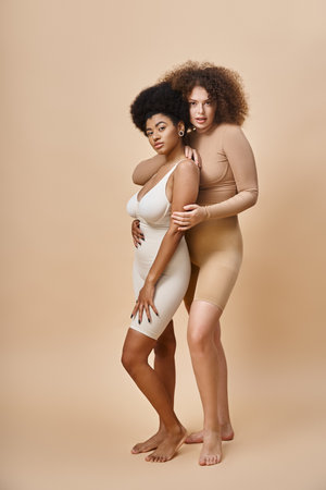 confident multicultural body positive women in underwear standing on beige, natural plus size beautyの写真素材