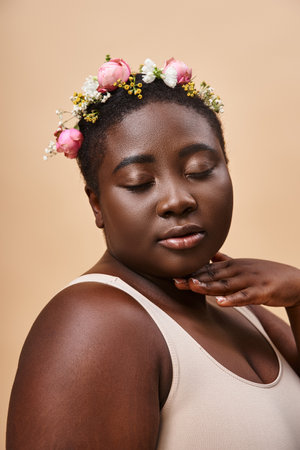 portrait of african american plus size woman with colorful flowers in hair and closed eyes on beigeの写真素材