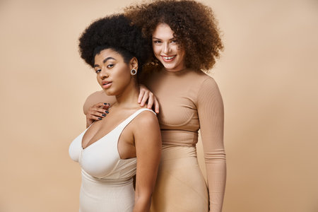smiling multicultural body positive women in underwear standing on beige, natural plus size beautyの写真素材