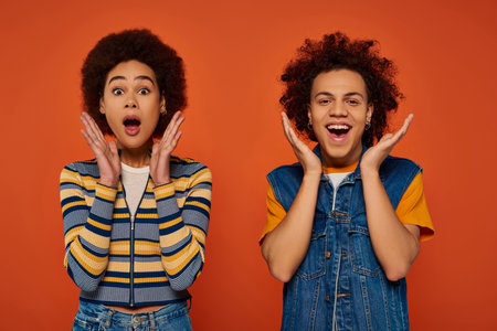 emotional african american siblings in vibrant outfits posing together on orange background, familyの写真素材