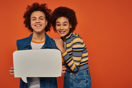 emotional caring african american brother and sister posing with speech bubble on orange backdropの写真素材