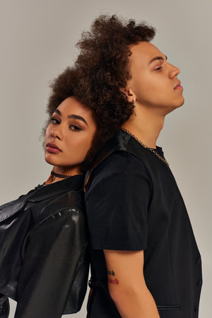 trendy young african american brother and sister in stylish clothes posing together on gray backdrop