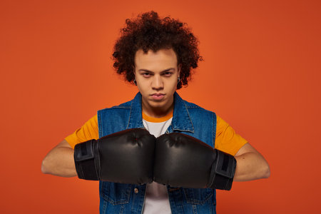 good looking sporty african american man posing actively in boxing gloves on orange backgroundの写真素材
