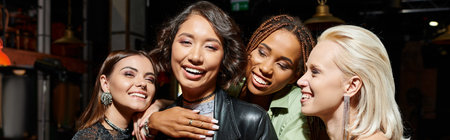 excited and vibrant multicultural female friends embracing in bar during party, horizontal banner
