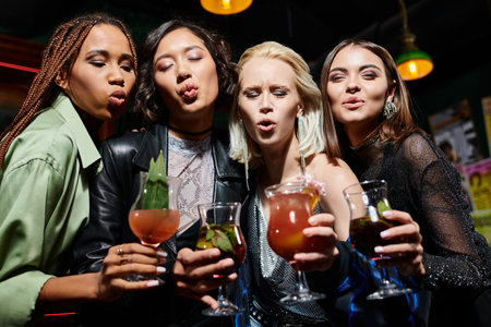 glamorous multiethnic girlfriends with cocktail glasses pouting lips while having fun in barの写真素材