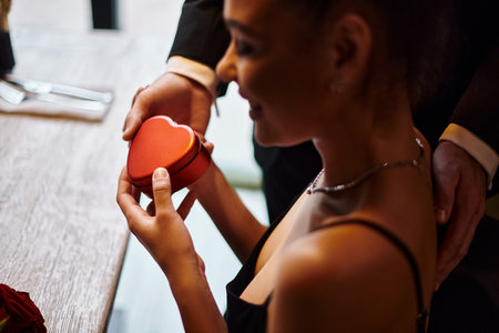 young man gifting heart-shaped box to happy african american girlfriend on Valentines dayの写真素材
