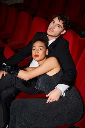 appealing multicultural couple in black elegant attires posing lovingly at cinema, Valentines day