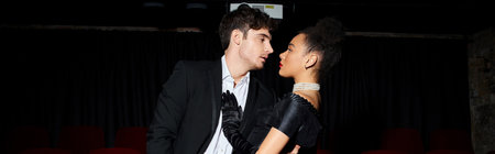 diverse caring couple in elegant black clothes hugging lovingly and looking at each other, banner