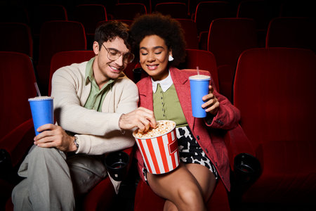 good looking cheerful diverse couple in stylish attires sharing popcorn at cinema, Valentines dayの写真素材