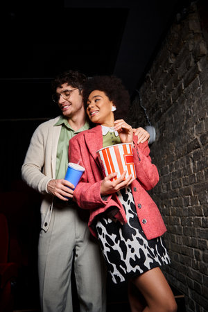 appealing cheerful diverse couple in trendy attire smiling while on date at cinema on Valentines dayの写真素材