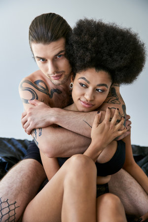 sexy interracial couple in underwear sitting on their bed and hugging lovingly, togethernessの写真素材