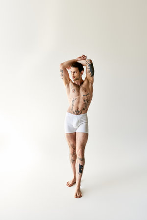 sexy attractive man with ponytail and cool tattoos in comfy underwear posing on ecru backgroundの写真素材
