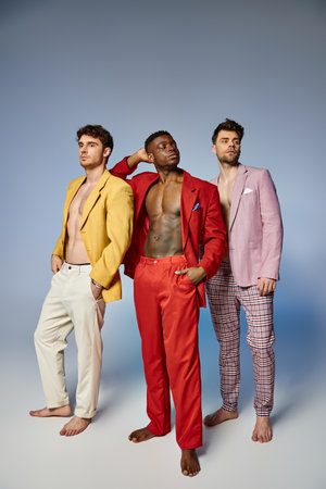 appealing sexy diverse men in unbuttoned vibrant suits posing on gray backdrop, fashion conceptの写真素材