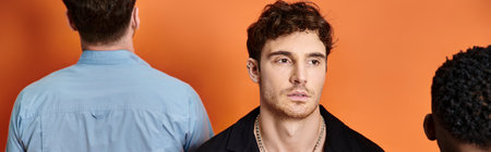 focus on young man in street attire looking at camera with back view of his diverse friends, bannerの写真素材