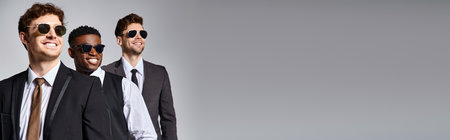 jolly diverse friends in business attire with sunglasses posing together on gray backdrop, bannerの写真素材