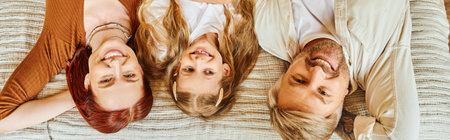 top view of joyful parents and daughter lying down on bed and looking at camera, horizontal banner