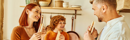 cheerful parents and cute son eating sandwiches for breakfast in modern kitchen, horizontal banner