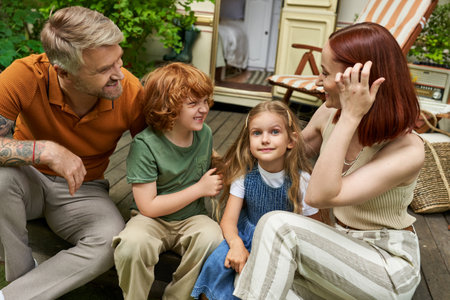 smiling parents talking to daughter and son while sitting near trailer home, bonding moments