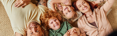 top view of cheerful parents and children lying down on floor in living room, horizontal banner