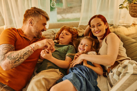 cheerful parents with joyful kids relaxing and having fun on soft bed in cozy trailer home, leisureの写真素材