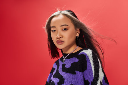 beautiful young asian model in vibrant sweater with animal print with heart shaped necklace on red
