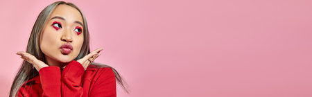 pretty asian young woman with heart shape eye makeup pouting lips and looking away on pink, bannerの写真素材