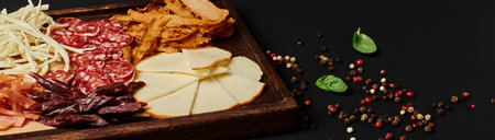 charcuterie board with gourmet cheese selection, dried beef and salami slices on black, banner