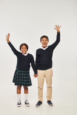 excited preteen african american schoolchildren in uniform holding hands on grey backgroundの写真素材