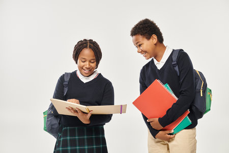 happy african american children in school uniform holding textbooks and standing on grey backdropの写真素材