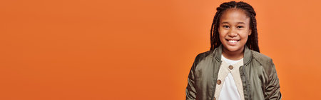 happy african american girl with braids in winter attire smiling cheerfully at camera, bannerの写真素材