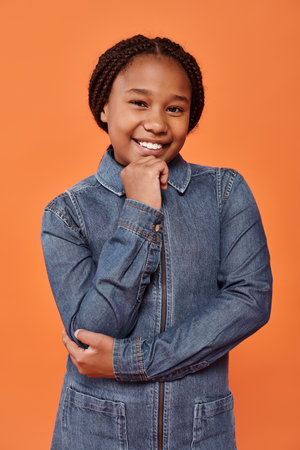 positive african american girl with braids smiling and looking at camera on orange backdrop
